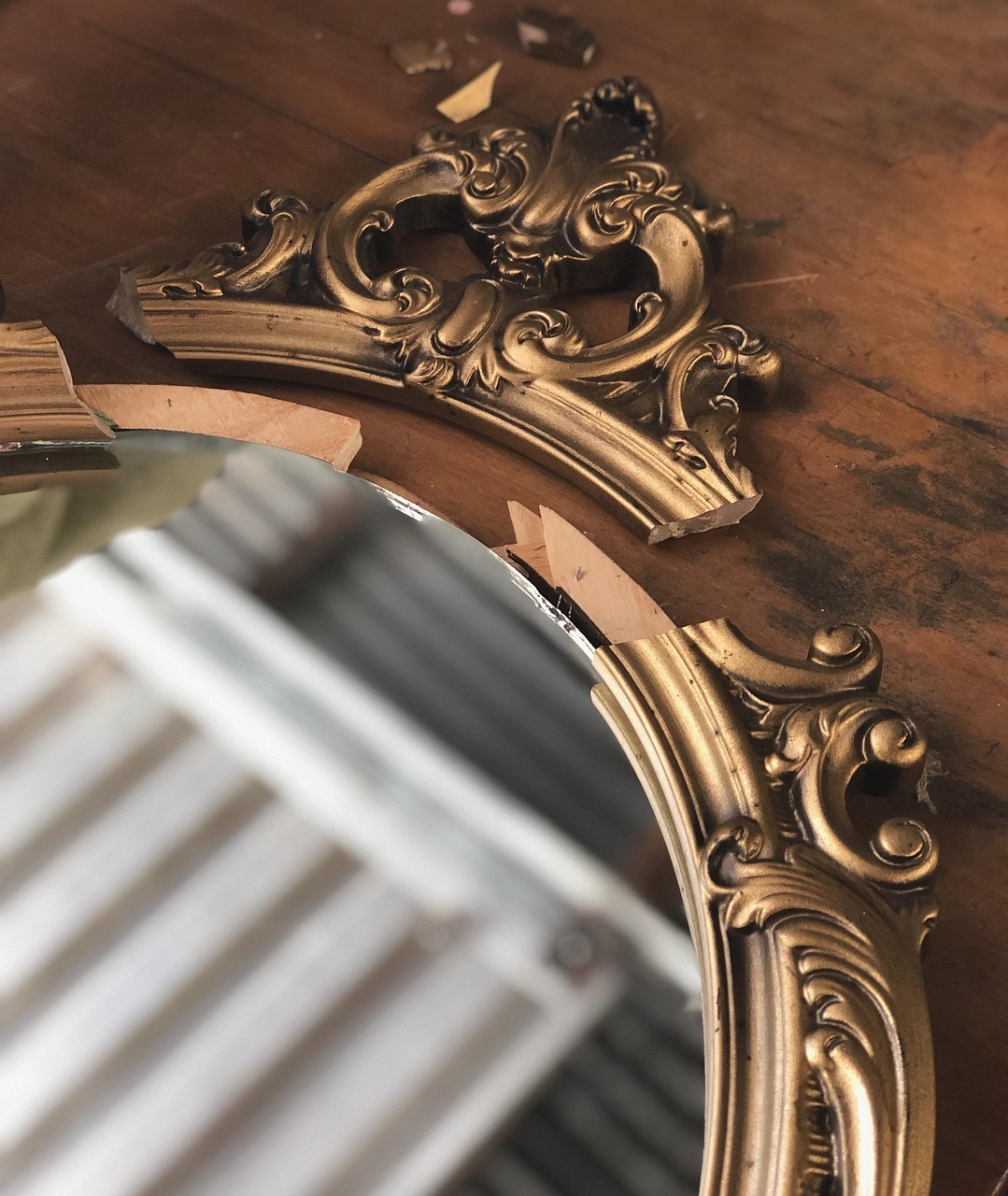 A carved gold-toned mirror frame curves across a wooden wall, reflecting bright diagonal bands from a nearby window or blind.